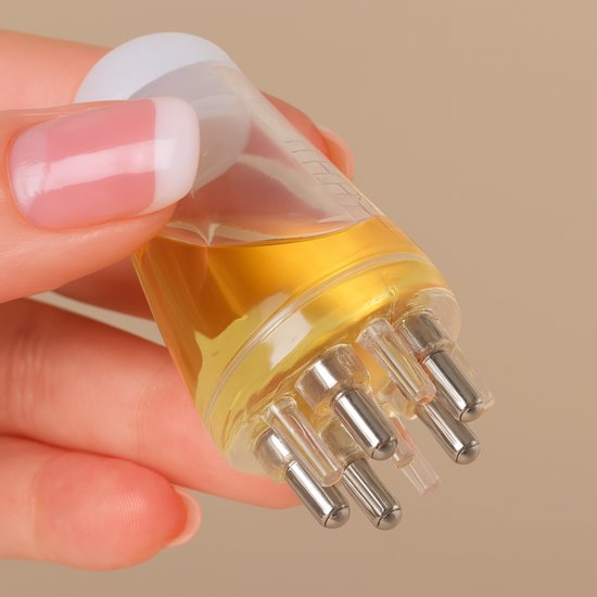 Hand met nagels die een transparante olie applicator vasthoudt, gevuld met gele olie.