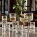 Verres à motif losange, dont un grand verre avec de l'eau, un verre à vin avec une boisson ambrée et des coupes.