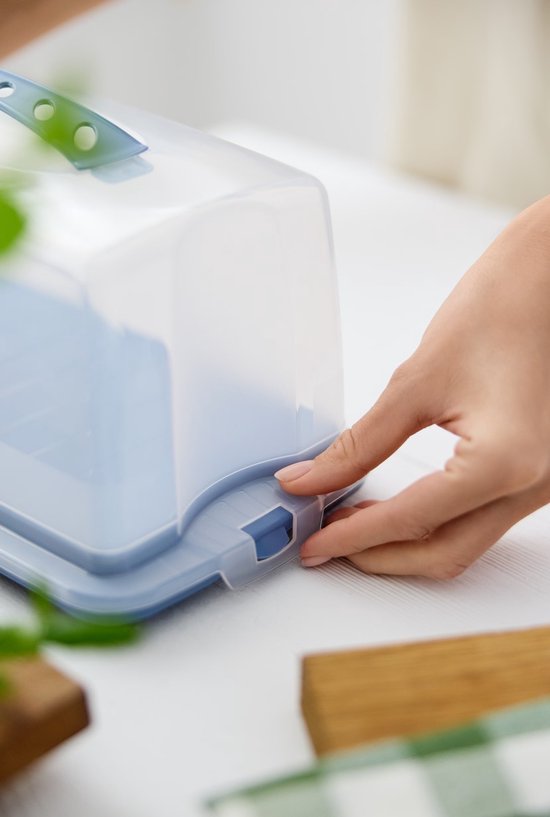 Een hand sluit de blauwe clips van een transparante taartdoos.