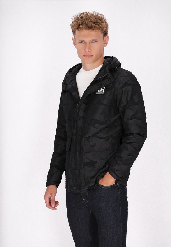 Model in een zwarte camouflageprint jas met capuchon, wit T-shirt en spijkerbroek.