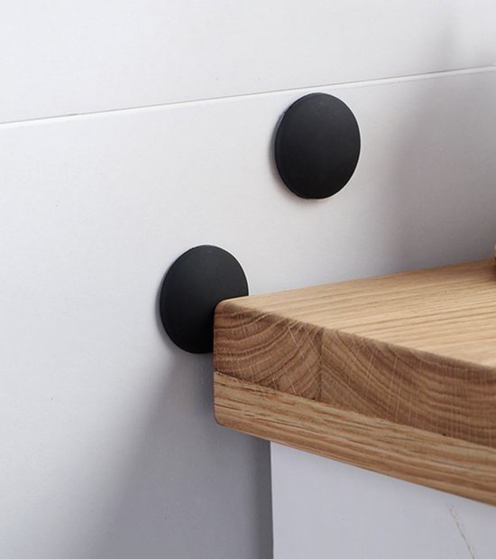Twee ronde, zwarte deurstoppers tegen een witte muur naast een houten plank.