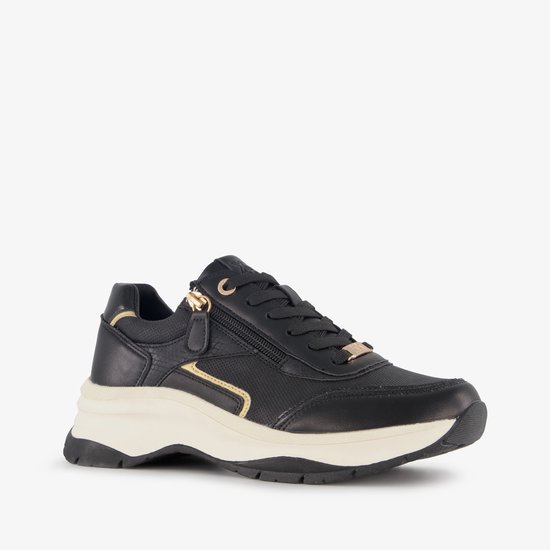 Zwarte sneaker met gouden rits en details, witte zool, van de zijkant gezien.