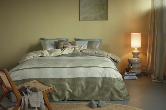 Lit fait avec une housse de couette verte à rayures et divers coussins dans une pièce faiblement éclairée.