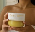 Een persoon houdt een geel potje 'Lemon Zest Body Scrub' van The Ceel vast.