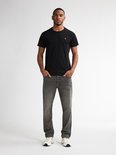 Man in een zwarte T-shirt met korte mouwen en een grijze jeans.