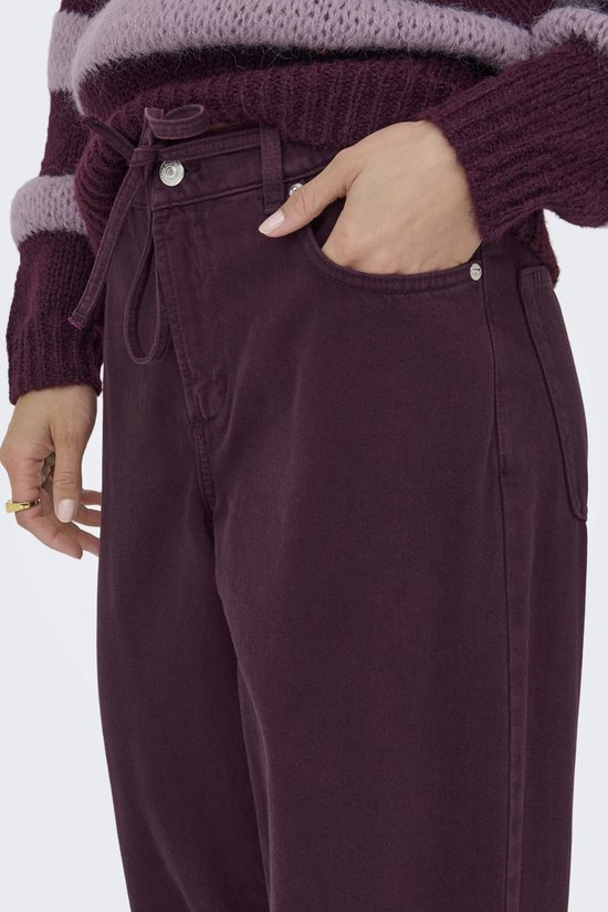Close-up van een model met paarse wijde broek, met trekkoord en strik. Draagt een gestreepte trui.