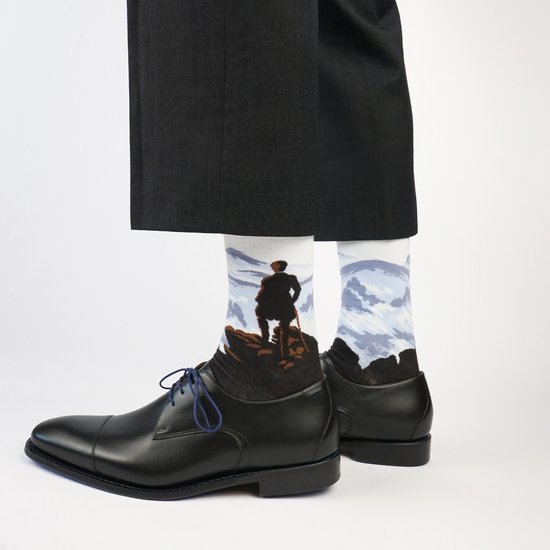 Witte sokken met een man op een rots, uitzicht op bergen, met zwarte schoenen.