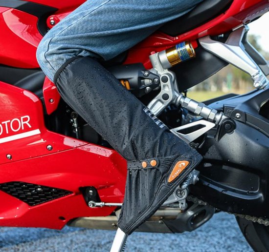 Zwarte hoge regenlaars-overtrekken met oranje knopen en reflecterende details, gedragen door een persoon op een motorfiets.