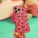 Rode telefoonhoes met witte bloemenpatroon, vastgehouden door handen met gele nagellak.