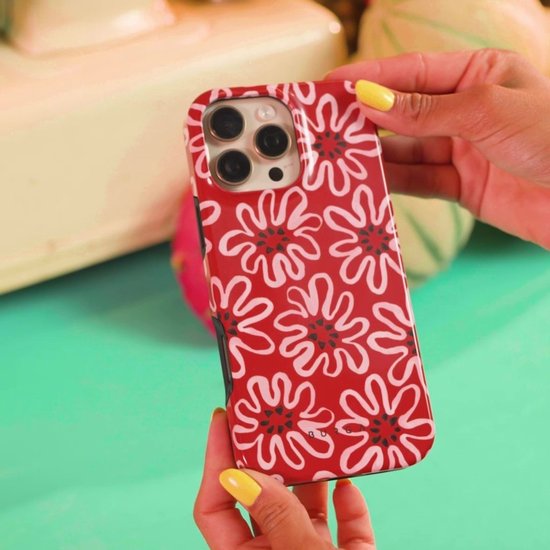 Rode telefoonhoes met witte bloemenpatroon, vastgehouden door handen met gele nagellak.
