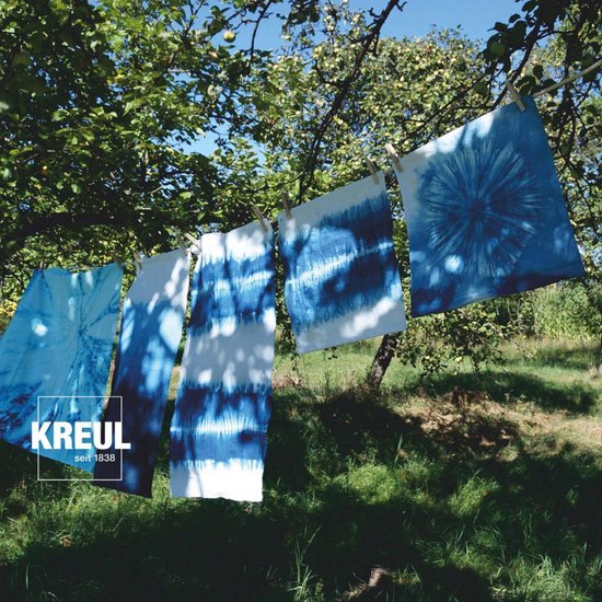 Cinq pièces de tissu bleu à imprimé batik sèchent sur une corde à linge dans un jardin.