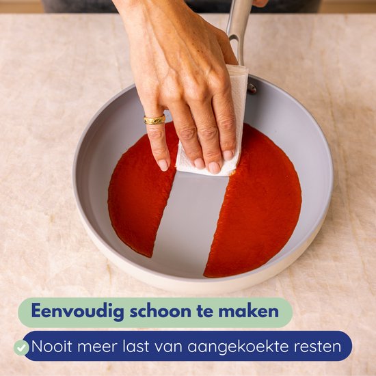 Hand veegt rode saus uit een grijze koekenpan met een witte doek. Tekst: Eenvoudig schoon te maken, nooit meer last van aangekoekte resten.