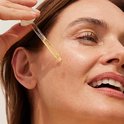 Close-up van een druppel Nuxe Super Serum die uit een pipet valt op een gezicht.