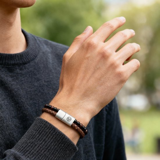 Man draagt een donkergrijs vest en een armband met bruine en zwarte kralen en een metalen sluiting.