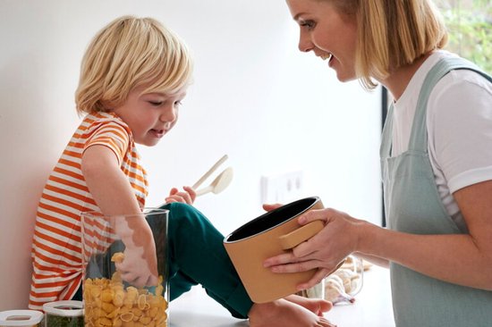 Mère et fils joyeux près d'une grande boîte de conservation remplie de pâtes. Le fils en sort quelque chose.