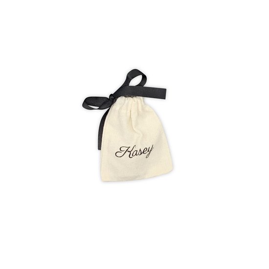 Crèmekleurig stoffen zakje met Kasey logo en zwart strikje.