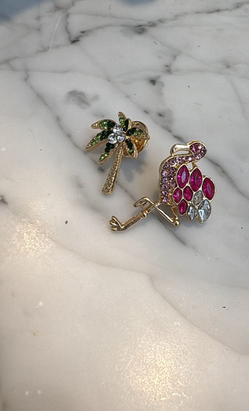 Gouden broche met een palmboom van groene en witte steentjes, en een flamingo van roze en witte steentjes.