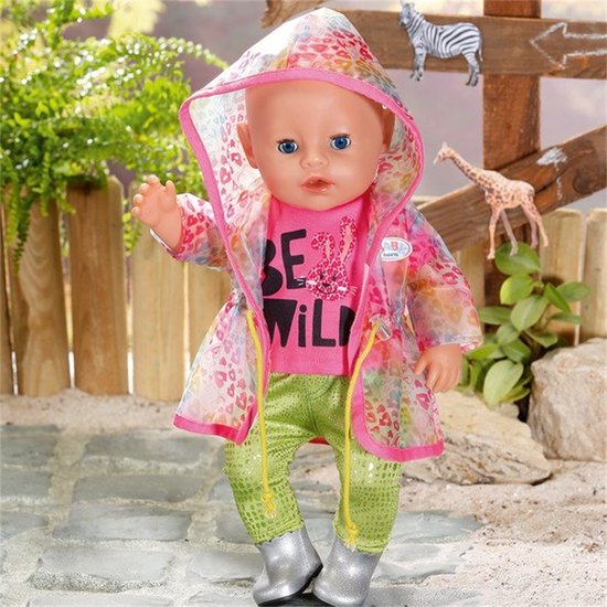 Baby pop met roze 'BE WILD' shirt, groene broek, zilveren laarsjes en een doorzichtige regenjas met regenboogprint.