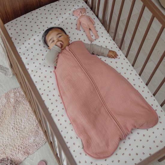 Baby in een roze slaapzak in een bedje met panterprint.