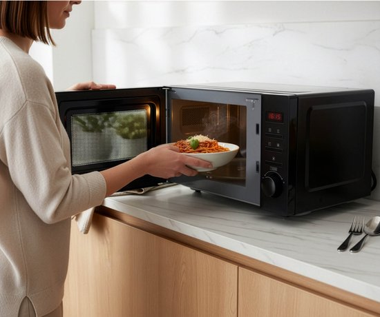 Une femme place une assiette de spaghettis fumants dans un micro-ondes noir Tomado ouvert.