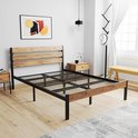 Bedframe met houten hoofdbord, zwart metalen frame, in een lichte slaapkamer met schilderij.