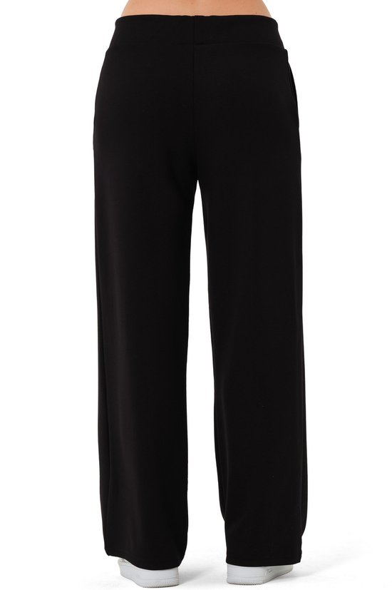 Achterzicht van zwarte wijde broek met rechte pijpen en witte sneakers.