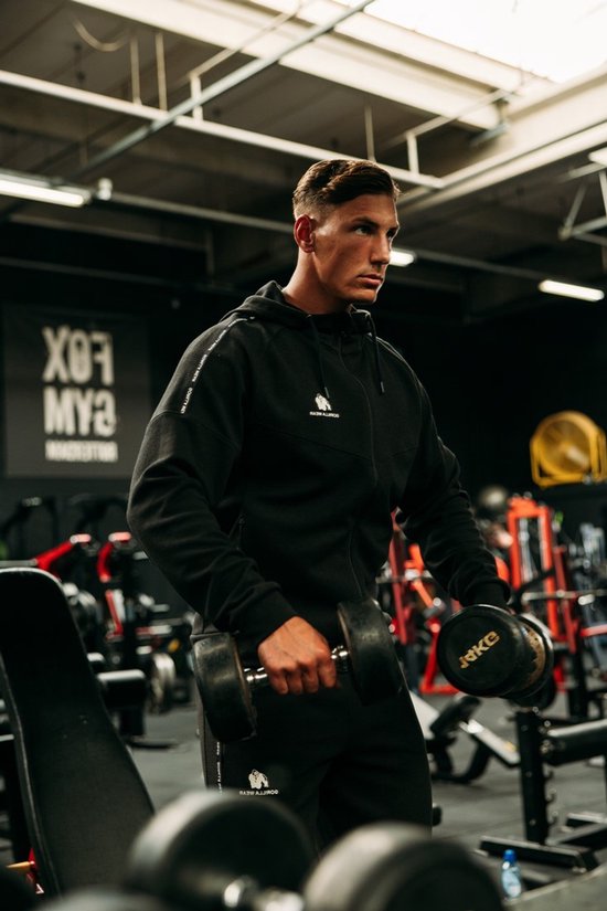 Man met spierbundel met een zwarte trainingsjas en trainingsbroek van Gorilla Wear, met dumbbells.