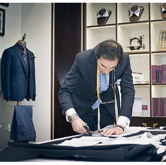 Kleermaker snijdt stof met een schaar in een atelier met kleding op mannequins.