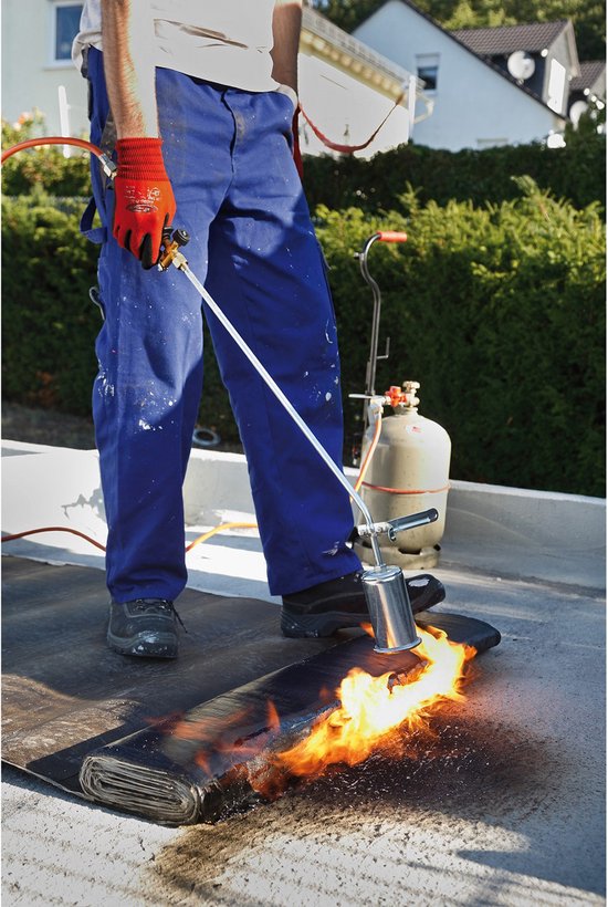 Man met rode handschoenen en blauw werkpak gebruikt brander op zwarte dakrol met vlammen.
