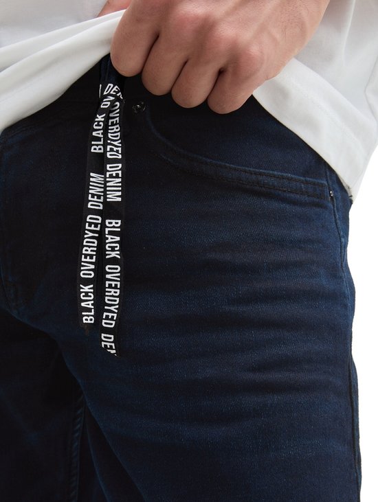 Detail van een donkerblauwe jeans met een trekkoord met "BLACK OVERDYED DENIM"-opdruk.