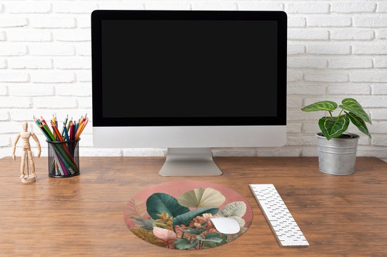 Ronde muismat met tropische bladeren print, roze ondergrond, op een bureau naast een monitor.