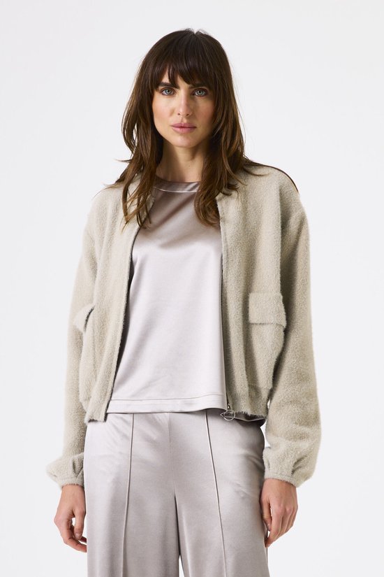 Mannequin portant un blouson bomber beige duveteux zippé avec un haut et un pantalon satinés gris argent.