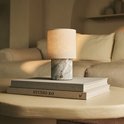 Marmeren tafellamp met linnen kap staat op een stapel boeken.