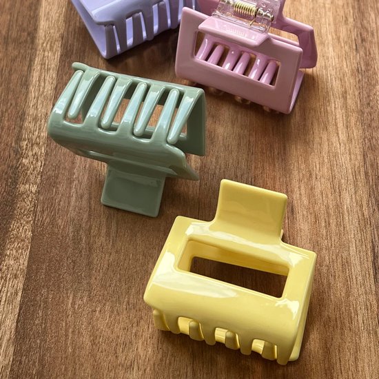 Vier pastelkleurige haarklemmen op een houten ondergrond: lichtgroen, lichtpaars, roze en geel.