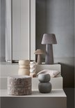 Stapelbare ronde bijzettafels van fiber clay in beige en grijs, naast decoratieve kussens.