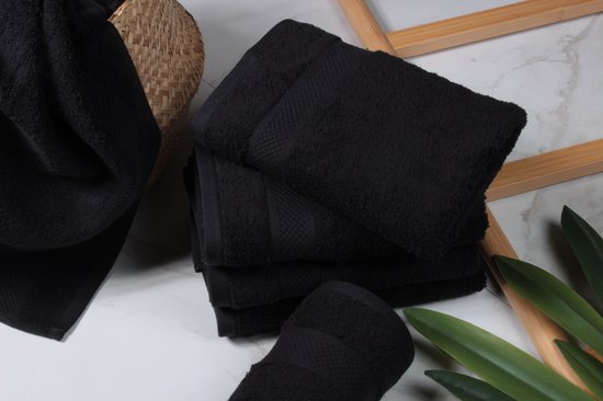 Zwarte handdoeken op een marmeren ondergrond met planten en een mand.