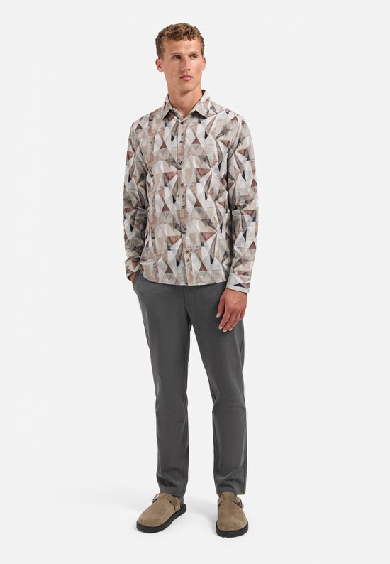 Man in lichtbruin corduroy overhemd met geometrisch patroon van bruine, grijze en witte driehoeken, en grijze broek, van voren.