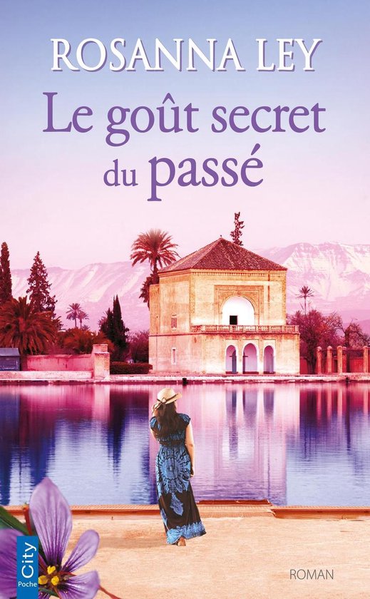 Couverture de livre : Femme avec un chapeau d'été se tient au bord de l'eau, avec un bâtiment orangé et des montagnes en arrière-plan.