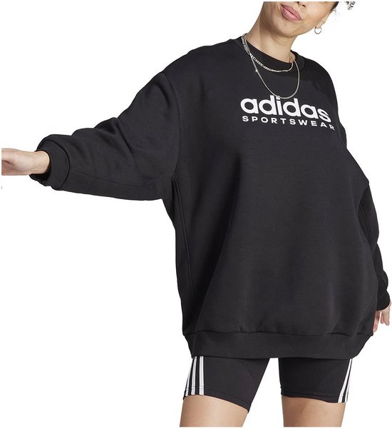 Vrouw in zwarte oversized Adidas sweater met 'adidas sportswear' logo.