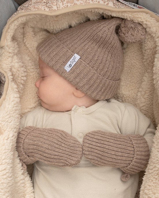 Baby met bruine gebreide muts met pompon en bijpassende wanten, in een warme omslagdoek.