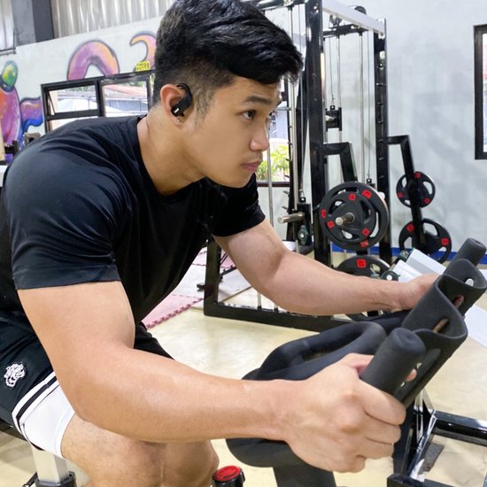 Man met zwarte oordopjes, sportend op een hometrainer in een sportschool.