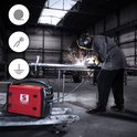 Rood Stamos lasapparaat in een industriële hal. Een lasser met een beschermende outfit last aan een metalen buis, vonken spatten.