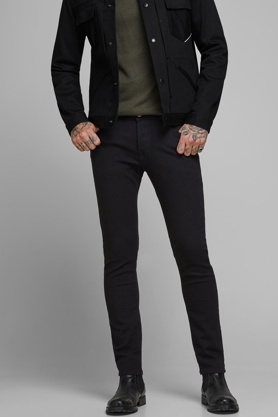 Man in een zwarte spijkerjas en zwarte skinny jeans, gedetailleerde weergave.