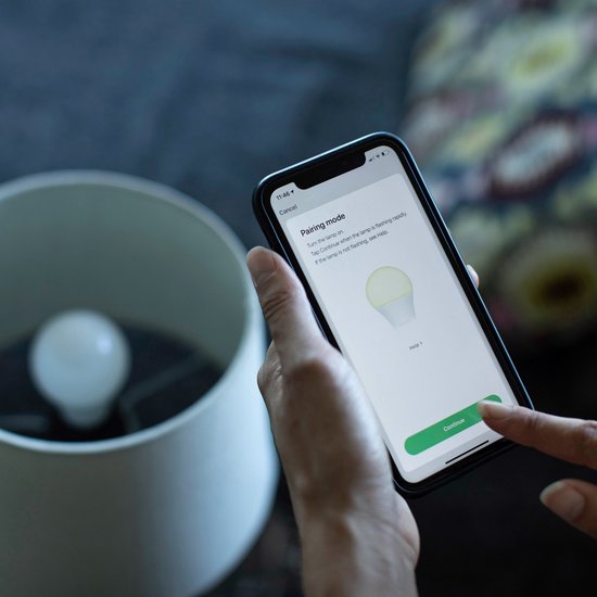 Hand houdt smartphone met de Hombli app in 'Pairing mode'. Een lamp is zichtbaar in de lampenkap.
