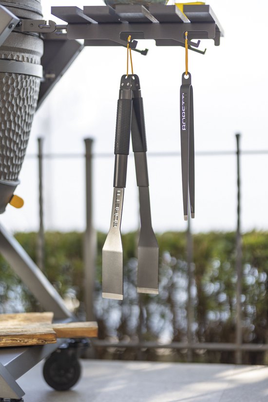 Twee zwarte barbecue tangen met gele lussen hangen aan een grill.