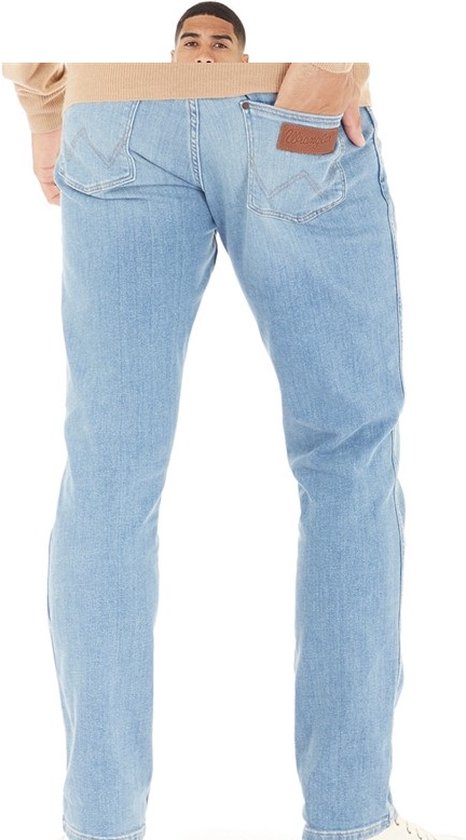 Man in een lichtblauwe spijkerbroek met bruin leren Wrangler logo op de achterzak.
