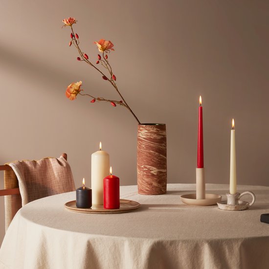 Vier brandende kaarsen op een tafel: twee hoge rode en crème kaarsen, twee korte zwarte en crème kaarsen. Een vaas met bloemen staat ernaast.