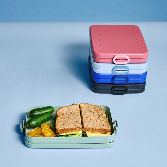 Gestapelde Mepal lunchtrommels in roze, lichtblauw, blauw en zwart. Een groene trommel met lunch ligt ervoor.