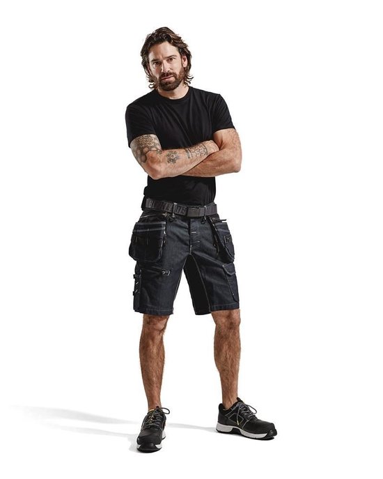 Man met gekruiste armen draagt een donkerblauwe werkshort met veel zakken, riem en zwarte t-shirt.