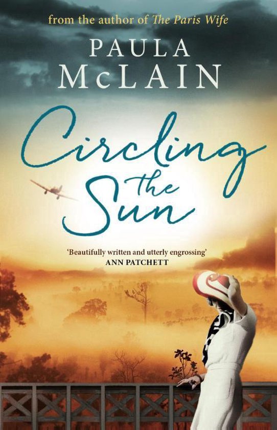 Boekcover 'Circling the Sun' van Paula McLain. Een vrouw in een witte jurk met een rode en witte hoed staat op een balkon met uitzicht op een mistige zonsondergang. Een vliegtuigje vliegt in de lucht.